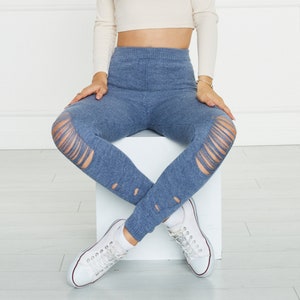 Puede incluir: Leggings de punto azul con dise&ntilde;o de cintura alta, textura acanalada y detalles de aberturas desgastadas en las rodillas y la parte inferior de las piernas. Los leggings se combinan con zapatillas de lona blancas y un top corto de manga larga.