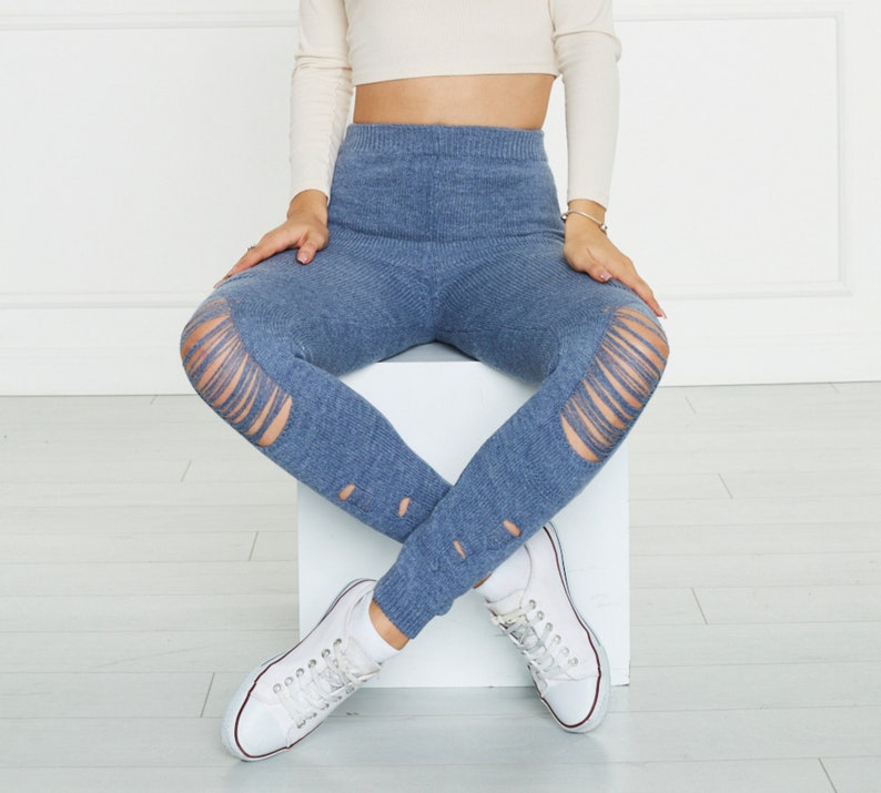 Puede incluir: Leggings de punto azul con dise&ntilde;o de cintura alta, textura acanalada y detalles de aberturas desgastadas en las rodillas y la parte inferior de las piernas. Los leggings se combinan con zapatillas de lona blancas y un top corto de manga larga.