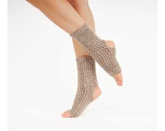 May include: A pair of beige, open-heel, and open-toe socks featuring a textured, diamond-shaped knit pattern. The socks have a ribbed cuff at the top and a ribbed band around the opening for the toes, providing a snug fit around the lower leg.