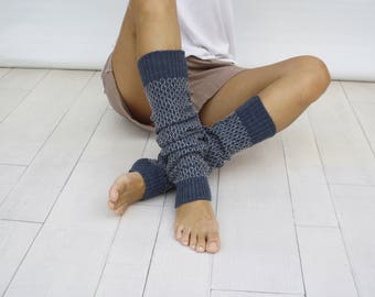 May include: A pair of dark blue knit leg warmers featuring a repeating white chain-link pattern. The leg warmers have ribbed cuffs at the top and bottom edges, providing a snug fit around the lower legs. The knit fabric has a textured appearance.
