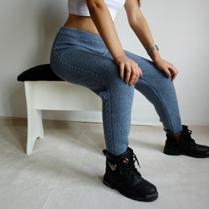 Three-quarter seated view showing the cable knit side panel of the denim blue leggings against contrasting black ankle boots.