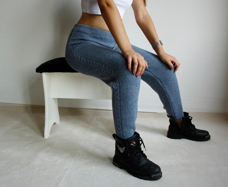 Three-quarter seated view showing the cable knit side panel of the denim blue leggings against contrasting black ankle boots.