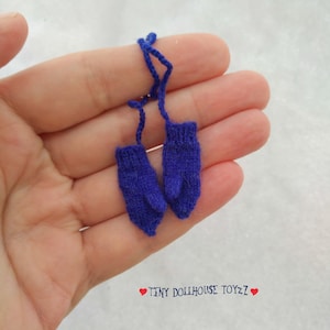 Könnte beinhalten: Ein Paar blaue gestrickte Puppenhaus-Handschuhe mit einem Schnürsenkel.