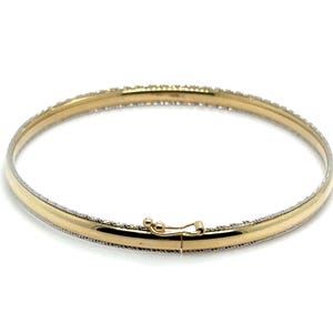 May include: A gold bangle bracelet with a hinged clasp. The bracelet has a smooth, polished gold center band and a textured, silver-colored border. The clasp is also gold-toned.