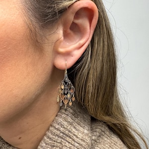 May include: Gold and silver tone dangle earrings with a cascading design of small, round, and oval shapes.