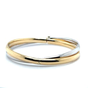 Könnte beinhalten: Ein gold- und silberfarbenes Armreif-Armband. Das Armband hat ein goldenes Band, das ein silbernes Band kreuzt. Das Armband hat einen Verschluss. Der Schmuck wird auf weißem Hintergrund präsentiert.