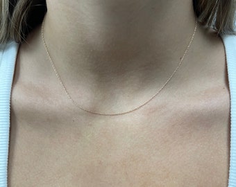 May include: A simple gold chain necklace on a person's neck.
