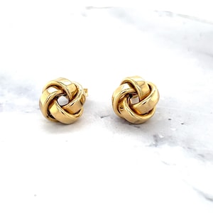 May include: A pair of polished gold stud earrings featuring a three-dimensional knot design. Each earring is crafted from smooth, reflective metal shaped into an intricate, interconnected loop pattern that creates a rounded, sculptural form.