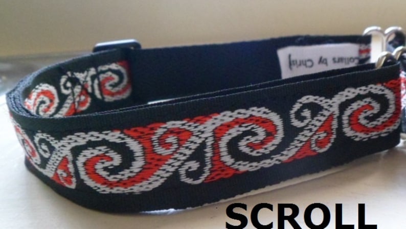 May include: Black dog collar with a red and white patterned design. The pattern features a repeating swirl design. The collar has a metal buckle and a metal D-ring.