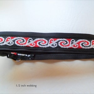 Puede incluir: Correa de guitarra negra con un diseño tejido rojo y blanco. La correa tiene 1,2 cm de ancho.