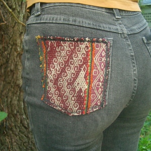 May include: Gray denim jeans with a colorful woven patch sewn on the back pocket.