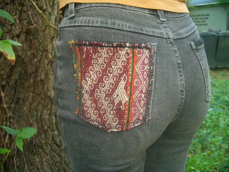 May include: Gray denim jeans with a colorful woven patch sewn on the back pocket.