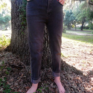 May include: A pair of dark gray denim jeans with a high waist and a straight leg fit. The jeans are cuffed at the bottom and the person wearing them is barefoot.