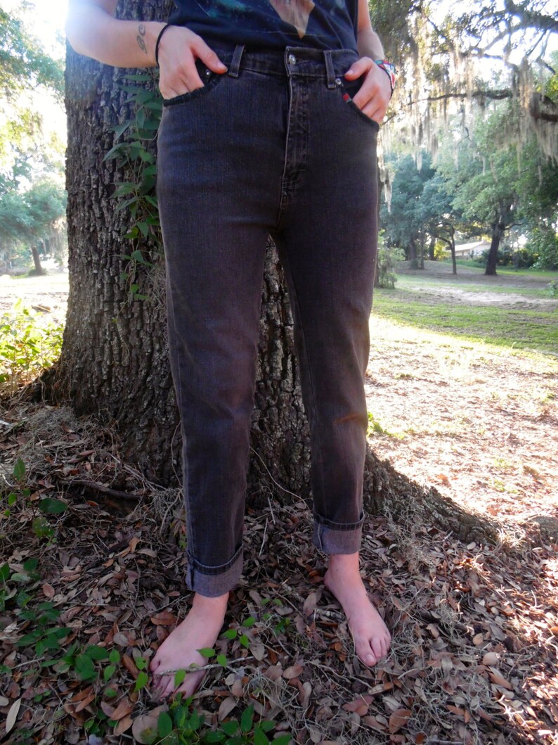 May include: A pair of dark gray denim jeans with a high waist and a straight leg fit. The jeans are cuffed at the bottom and the person wearing them is barefoot.