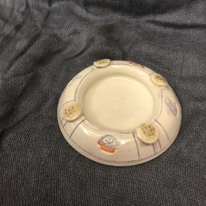 May include: White ceramic candle holder with a decorative design featuring small blue and yellow flowers and four round, raised, yellow and white designs.