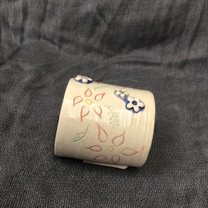 May include: White ceramic mug with a floral design. The flowers are red, yellow, and blue. The mug is decorated with a textured surface.