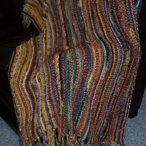 May include: A striped crocheted throw blanket with a fringe border in shades of brown, gold, and purple.