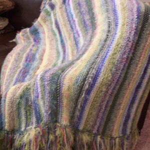 May include: A striped crocheted throw blanket with a fringe border in shades of green, blue, purple, and yellow.