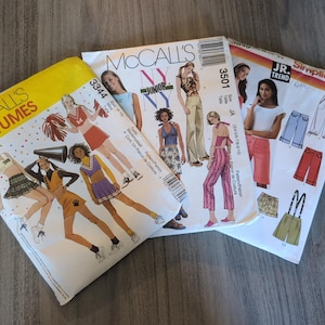 May include: Three paper sewing pattern envelopes featuring McCall's Costumes 3344 with cheerleader illustrations, McCall's 3501 NY NY Junior featuring various casual outfits, and Simplicity 3849 JR. Trend showing shorts, pants, and overalls illustrations.