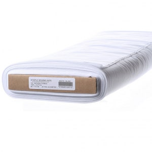 May include: A roll of white woven fusible fabric for sewing. The label reads "STAPLE SEWING AIDS 122 WOVEN FUSIBLE COTTON" and "45"/115 CM - 25 YDS/22.8 METER". The fabric is white and appears to be cotton.