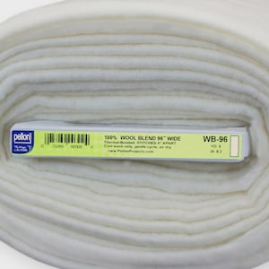 May include: A rolled bolt of off-white 100% wool blend fabric. The label reads "100% WOOL BLEND 36" WIDE". The fabric is tightly rolled, showing the layers of material. The label also includes the text "WB-96".