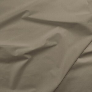 May include: A close-up of a smooth, light brown fabric with a subtle sheen. The fabric is folded and draped, creating soft folds and wrinkles.