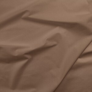 May include: A close-up of a smooth, brown fabric with soft folds and wrinkles.