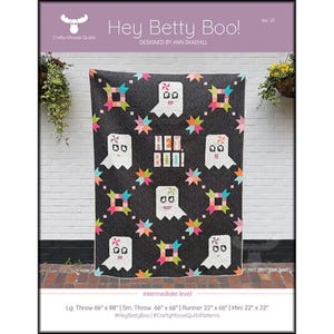 May include: A black quilt featuring white ghost designs and colourful starburst patterns. The quilt is titled "Hey Betty Boo!" and designed by Ann Skaehill. The large throw size is 168cm x 224cm.