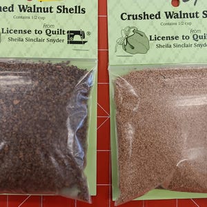 May include: Two clear plastic bags filled with crushed walnut shells. The bags are labeled "Crushed Walnut Shells" and contain 1/2 cup each. The bags are from "License to Quilt" by Sheila Sinclair Snyder.