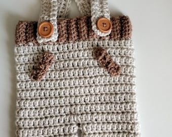May include: Beige crocheted baby overalls with brown trim and wooden buttons.