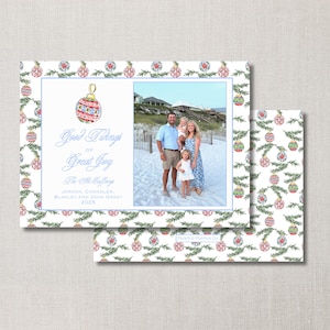 May include: Christmas card with a family photo and a festive ornament design. The card features the text "Good Tidings of Great Joy" and family names. The border has a repeating pattern of ornaments and greenery.