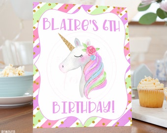 May include: A pink, green, and gold striped sign with gold glitter dots. The sign says "Blair's 6th Birthday!" and features a white unicorn with a rainbow mane and a pink flower crown.