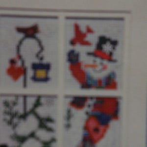 Puede incluir: Un patrón de punto de cruz que presenta un diseño de ventana con cuatro paneles. Cada panel muestra imágenes con temática invernal, incluyendo muñecos de nieve, pájaros y un árbol de Navidad. El texto "SIMPLY SEASONAL WINDOWPANE" está en la parte superior.