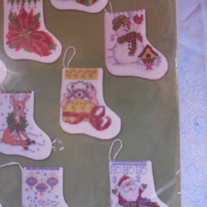 May include: A set of 10 cross-stitch patterns for Christmas stockings. The patterns feature a variety of holiday themes, including a snowman, a penguin, a reindeer, Santa Claus, and a poinsettia.