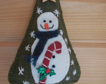 May include: A felt Christmas tree ornament with a snowman design. The snowman is wearing a blue scarf and a red and white candy cane. The tree is decorated with a wooden star and white snowflakes.