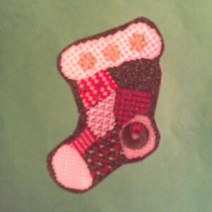 May include: A patchwork Christmas stocking with red, green, white, and brown fabric squares. The stocking has a white cuff with the words "Merry Christmas" embroidered in brown thread.
