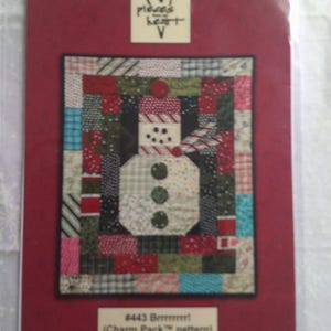 Könnte beinhalten: Eine rote Verpackung mit einem Patchwork-Schneemann-Design. Der Schneemann besteht aus verschiedenen Stoffmustern in Rot, Grün, Schwarz und Weiß. Die Verpackung enthält den Text "#443 Brrrrrr!" und "(Charm Pack pattern)". Das Logo "pieces of heart" befindet sich oben.
