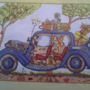 Può includere: Illustrazione a punto croce di un'auto blu d'epoca carica di bagagli e un cestino sul tetto. Un cane è all'interno dell'auto. La scena è ambientata in un ambiente naturale con alberi e uno sterrato. I sedili dell'auto sono rossi.
