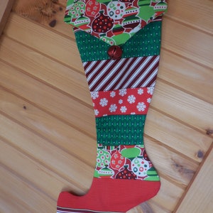 May include: A red and green Christmas stocking with a patchwork design featuring baubles, stripes, and snowflakes. The stocking has a bell at the top.