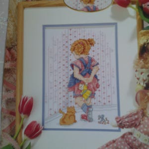 May include: A cross-stitch pattern featuring a girl in a pink and blue dress standing in a room with a cat and a toy. The title of the pattern is "Girl's Time Out".