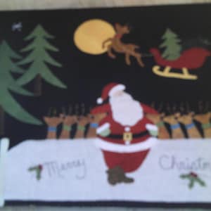 Può includere: Un calzino di Natale in feltro con un Babbo Natale rosso e bianco, renne che tirano una slitta e un albero di pino verde. Il calzino ha la scritta "Merry Christmas".