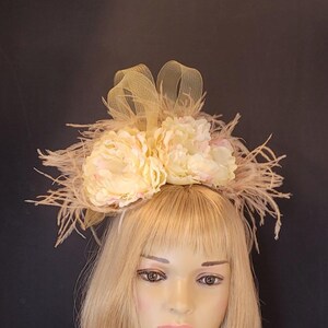 May include: A yellow and white flower headband with feathers and a tulle bow. The headband is worn on a mannequin with blonde hair.