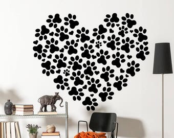 May include: Black and white wall decal of paw prints arranged in the shape of a heart. The decal is on a white wall with a shelf and other decor.
