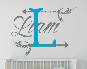 May include: A blue letter L with grey arrows and feathers on either side. The name Liam is written in cursive above the letter L.