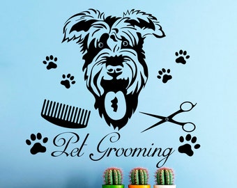 May include: Black and white silhouette of a dog with a comb and scissors, with the text "Pet Grooming" below. There are paw prints on either side of the text. The image is on a light blue wall with three potted plants on a white shelf below.