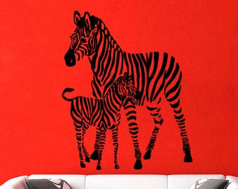 May include: Black and white silhouette wall decal of a zebra and a zebra foal. The zebra is standing with its head turned to the side, and the foal is standing next to it. The decal is on a red wall, and there is a white sofa in the foreground.