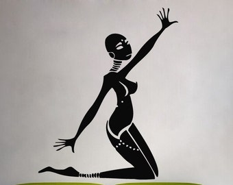 May include: Black silhouette wall sticker of a stylized kneeling figure with arms raised. The figure has a bald head and is wearing a decorative garment. The sticker is on a light grey wall above a lime green sofa.