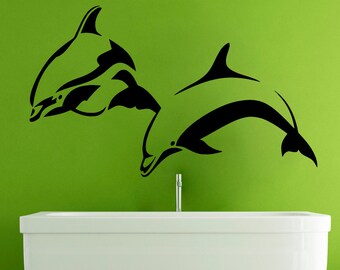 May include: Two black silhouette dolphins leaping out of the water, one in front of the other, on a green wall above a white bathtub.