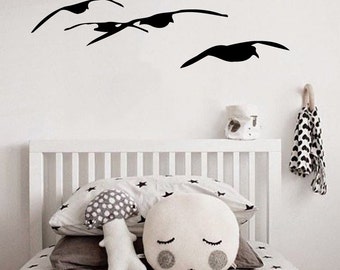 May include: A white cot with white and grey star patterned bedding. There are two pillows on the bed, one is a grey and white polka dot mushroom shaped pillow and the other is a white pillow with a face on it. There is a black bird silhouette wall decal on the wall behind the cot.