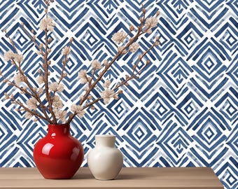 May include: A red vase and a white vase with floral branches on a wooden table. The background features a blue and white geometric pattern. The vases are the focal point, adding a pop of colour against the patterned backdrop.